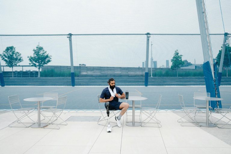 Man seated outdoors with prosthetic leg, embracing body positivity. Cityscape background.