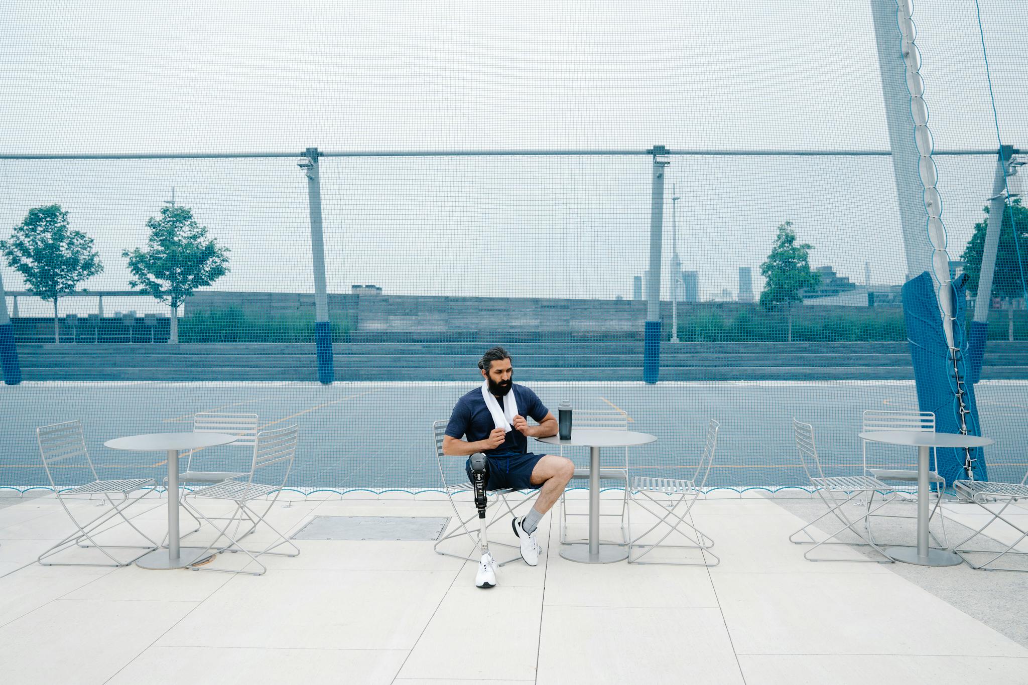 Man seated outdoors with prosthetic leg, embracing body positivity. Cityscape background.